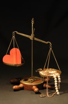 Red paper heart and various jewelry lying on old brass weight scale