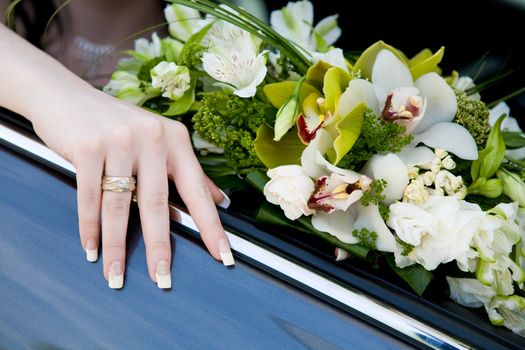 hand of the bride with wedding ring on the car and flower bouquet