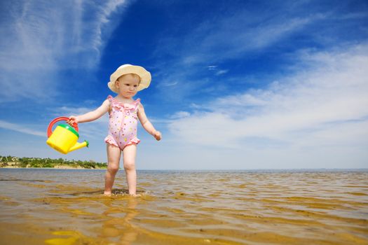 small girl with watering-pot on the seashore