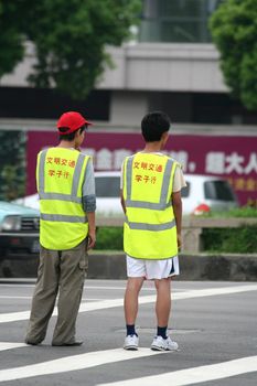 Two chinese teenagers helping pedestrians to cross the road