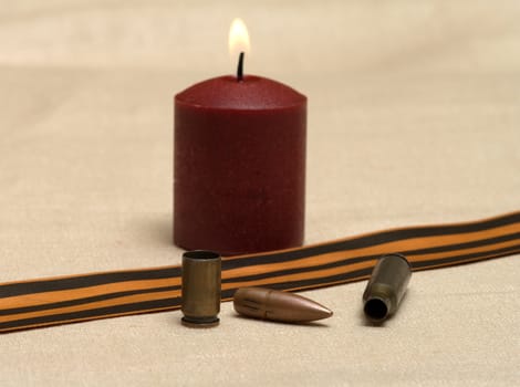 Burning candle, shell, bullet and St. George ribbon closeup.