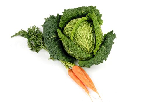 Single green cabbage with a bunch of raw crunchy orange carrots on a reflective white background