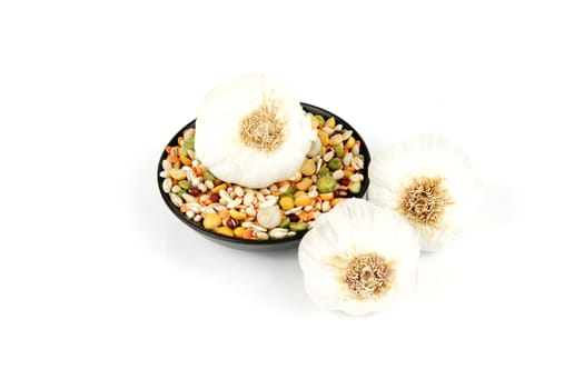 White raw garlic bulbs with a small black dish of soup pulses on a reflective white background