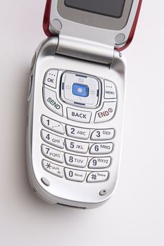 close up on the keypad of a red and silver cellular phone open with a blank screen