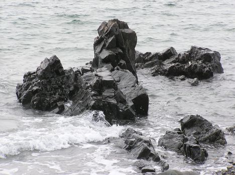 Waves crash over black rocks on a Maine Beach