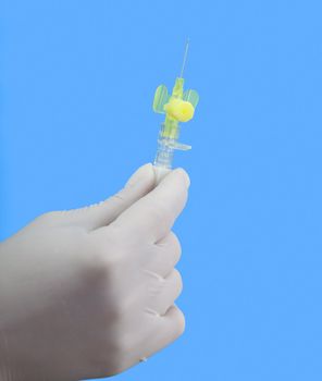 Hand in surgical glove holding a small intravenous needle against a blue background.