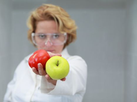 Image of a female researcher offering a tomatoe and an apple to suggest the ideea that healthy eating is recommended also by scientists.Specific lighting for a classical research laboratory.