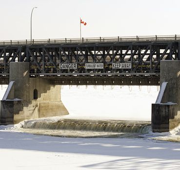 Close-up view of an open water dam in the winter, with a large sign telling people to stay away because of turbulent water.
