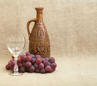Clay bottle, grapes and a glass on the background of canvas