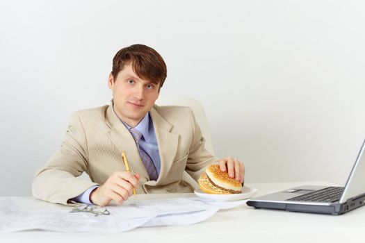 Young businessman is going to eat a delicious sandwich without interrupting work