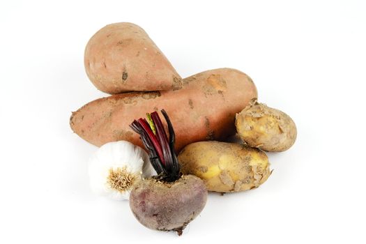 Two raw unpeeled sweet potatoes with garlic, brown potatoes and beetroot on a reflective white background