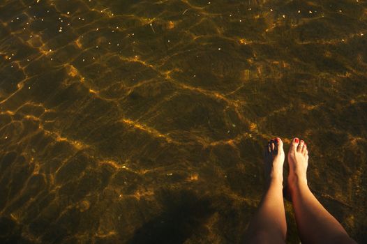 Beautiful lake scene with woman's legs dangling from boat dock.