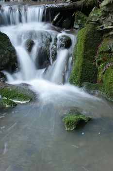 brook with small waterfall and stones with moss