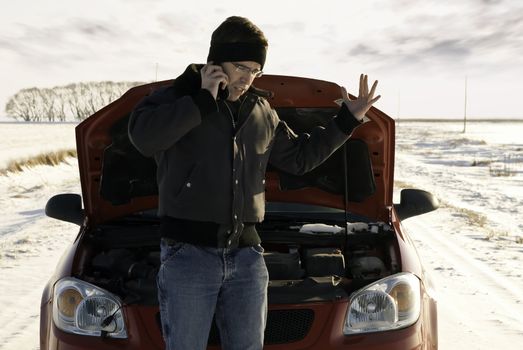 A frustrated young man is calling for help on his cell phone because his car broke down.