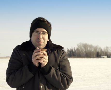 A young man warming his hands on a cup of coffee while standing outside in the winter.