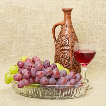 Still life with ceramic bottle, grape and glass on canvas background