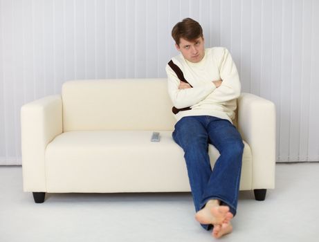 A gloomy man sitting on the couch in front of the TV