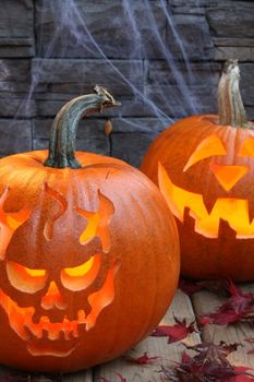 Carved pumpkins, 2 lit against brick and spider web