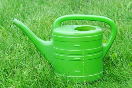 A green watering can on the green grass
