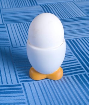 White egg in a plastic stand on a table covered with blue cloth.