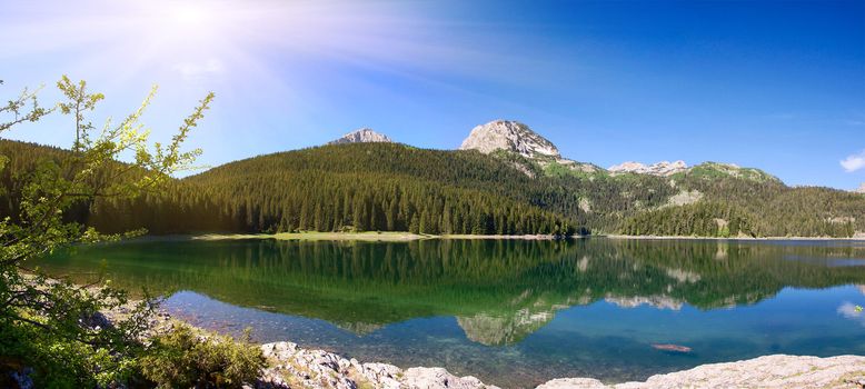 panorama of mountain lake with reflections and sunbeams
