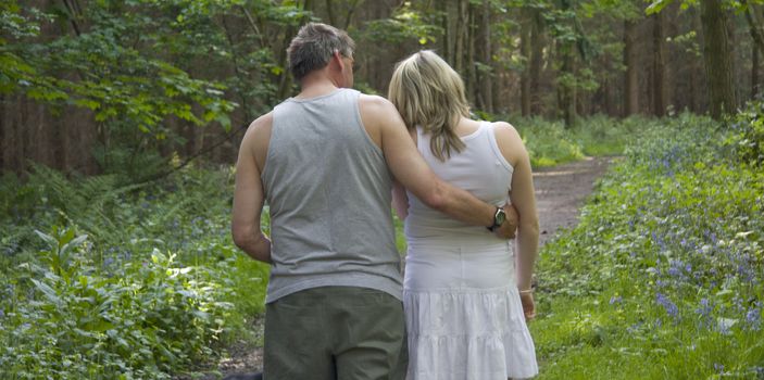 Couple walking arm in arm in the woods.