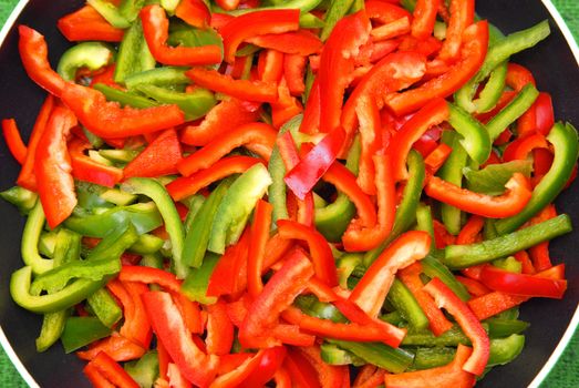 Green and red pepper on the frying pan