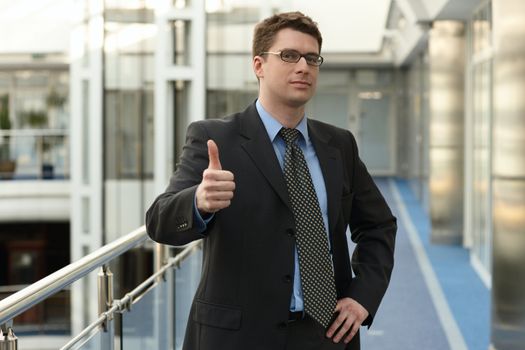 Portrait of young businessman in modern business office building corridor showing OK success