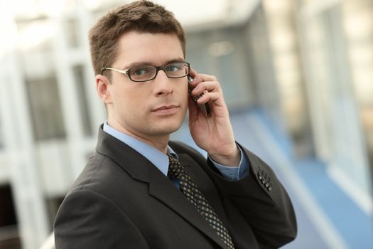 Portrait of young businessman talking on the cell phone in modern business office building corridor