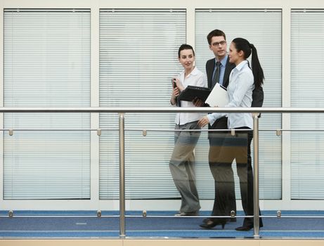 Business portrait of tree presons - young man and two women having nice chat talk on modern office corridor