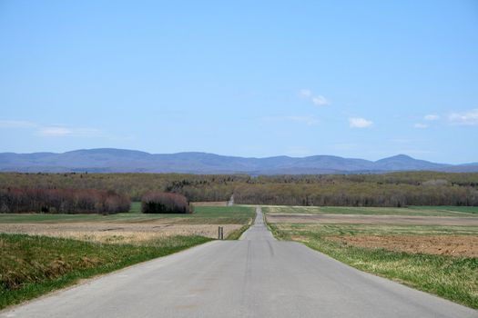 Country road crossing farmland and leading to mountains.