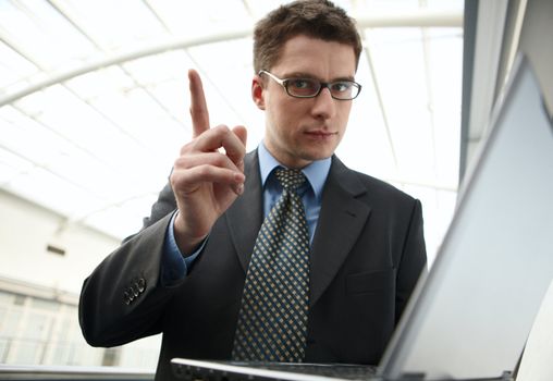 Portrait of young businessman in modern business office building corridor with up finger