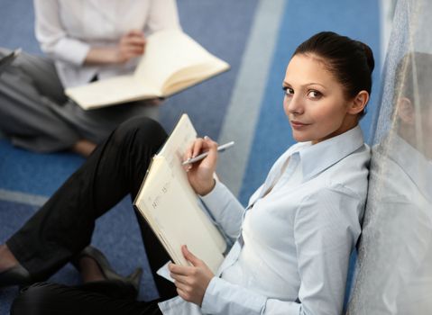 Portrait of young woman sitting with datebook on her lap in modern business office building corridor