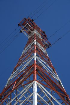 Red and white high voltage electricity pylon against the deep blue sky.