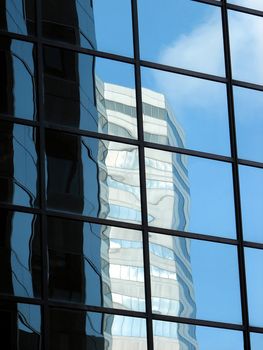 Glass-windowed corporate building reflecting another office tower and the blue sky.