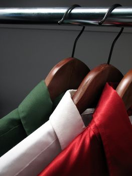 Colors of Italian flag: green, white and red shirts on wooden hangers in a closet.