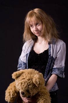 blonde girl on black handing teddy bear
