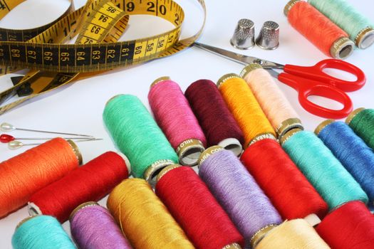 Colourful spools of thread, pins, thimbles, scissors and measure tape on white background.