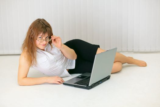Beautiful young woman with laptop lying on the floor