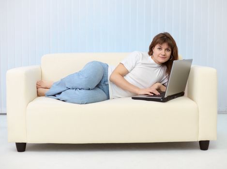 Beautiful young woman with laptop lying on sofa