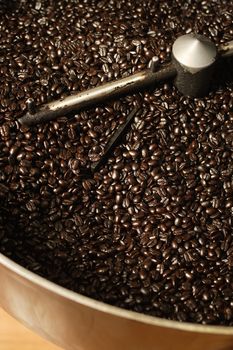 The freshly roasted beans from a large coffee roaster, just before the beans are stirred in the cooling cylinder. Beans are shiny from the natural oils after the dark roasting.

