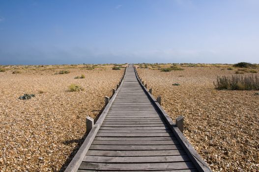 A raised wooden boardwalk across a pebble beach