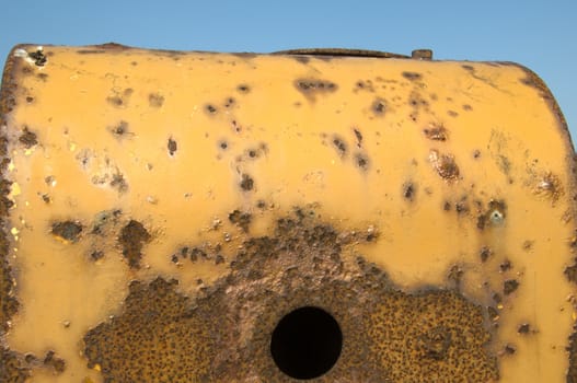 Part of a yellow rusty tractor, with blue sky in the background