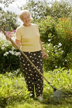 Smiling senior woman with rake in the garden