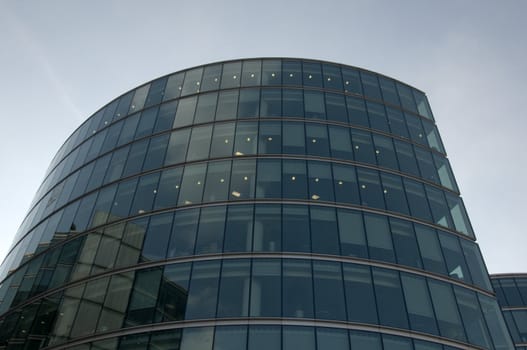 A glass office building in london with a cloudy blue sky