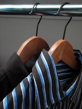 Two shirts of different colors on wooden hangers in a closet.