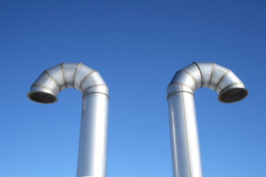 Two shiny metallic ventilation pipes on a blue sky background.
