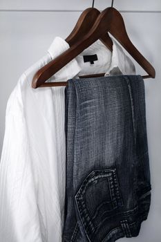 Man's clothing - blue jeans and white shirt on wooden hangers.