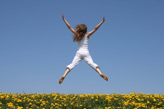 Girl in summer white clothes flying in a funny jump over flowering dandelion field.