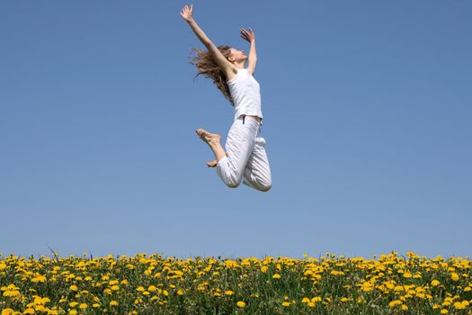 Girl in a happy jump "flying" over flowering dandelion field.